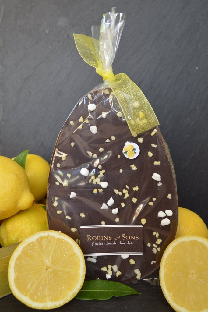 Sicilian Lemon Crunch easter Egg. Egg-shaped 70% dark chocolate flavoured with lemon oil and topped with lemon crystals ad meringue, in clear packaging and tied with yellow ribbon.