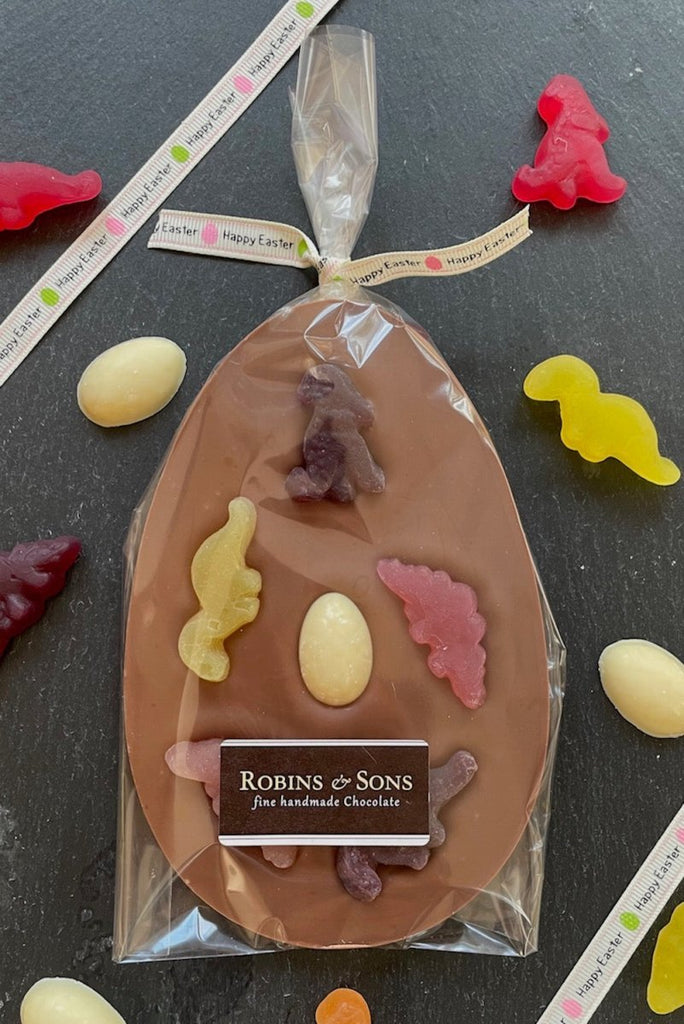 Dinosaur Easter Egg. Milk chocolate egg-shaped bar of chocolate topped with 5 fruit flavour dinosaur shapes in clear packaging with happy easter ribbon