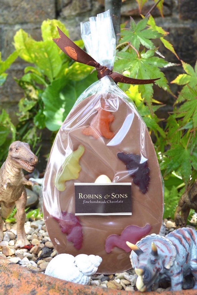 Dinosaur Easter Egg. Dinosaur themed milk chocolate easter egg bar topped with fruit flavour dinosaur shapes. In clear packaging and tied with ribbon