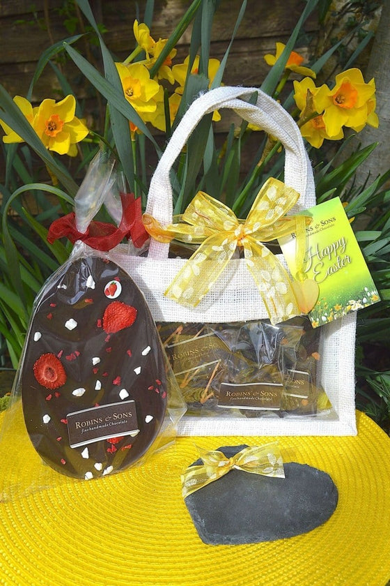 Easter dark chocolate gift bag. White jute gift bag tied with yellow ribbon and filled with dark chocolate treats and heart shaped drinks coaster