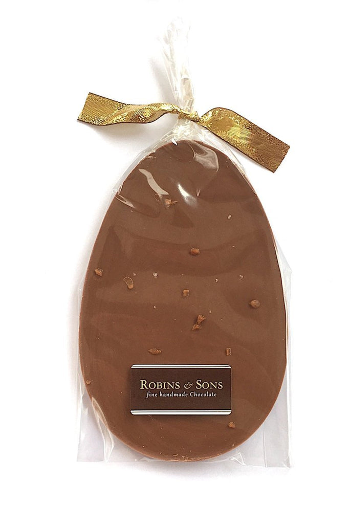 Salted Caramel Nibble Easter Egg. Egg-shaped milk chocolate bar topped with salted caramel pieces and sea salt flakes, in clear packaging tied with a gold ribon