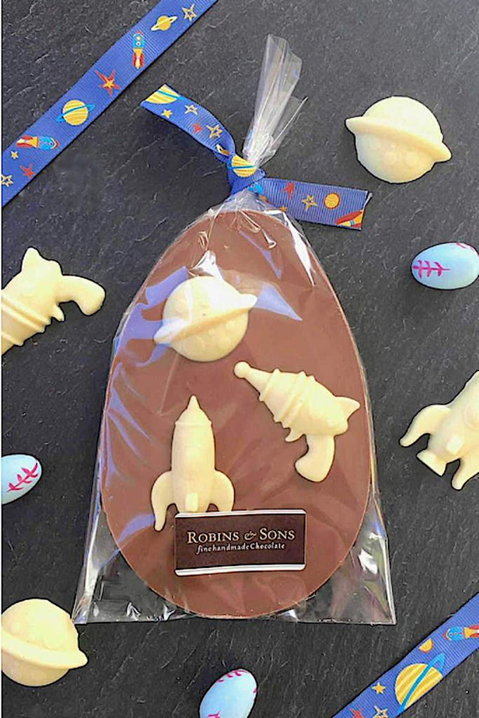 Space themed chocolate easter egg topped with space shapes in clear packaging with ribbon themed bow